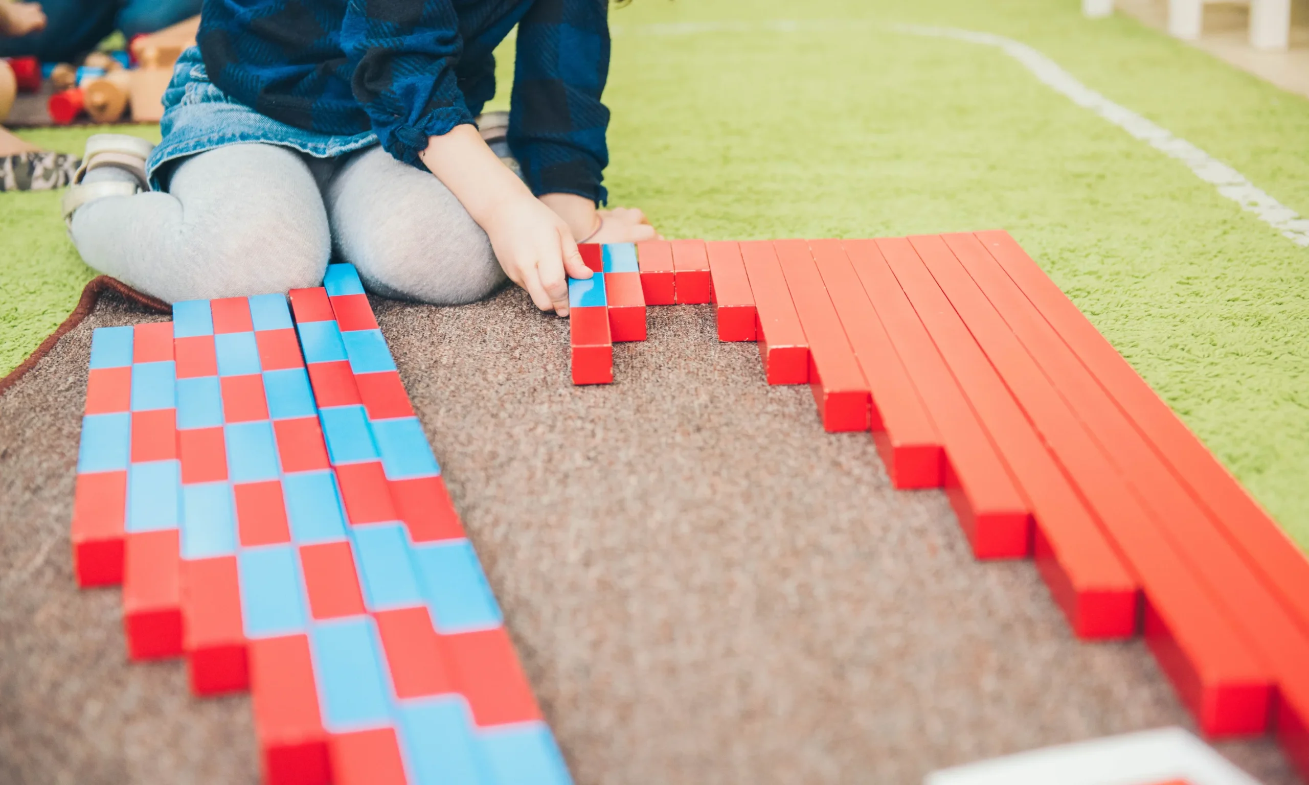 Child arranging red and blue Montessori number rods on a rug during a hands-on math activity.